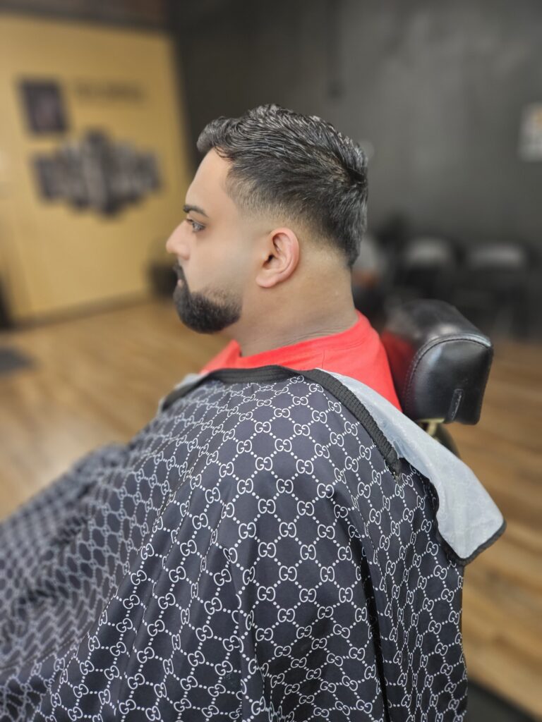 Hispanic man with fresh haircut and fade sitting in chair in barbershop